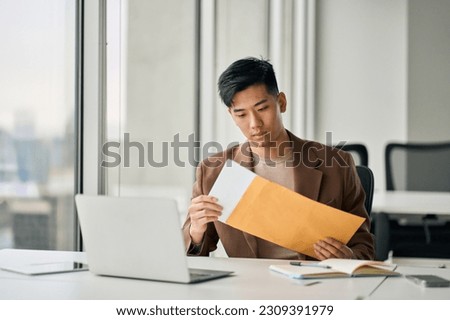 Young busy Asian professional business man manager opening envelope delivery receiving business mail letter holding paper documents bank statements, invoice file or bill sitting at desk in office. Royalty-Free Stock Photo #2309391979