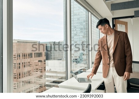Young busy Japanese businessman using laptop standing in office. Serious professional Asian business man executive managing data working on computer technology in corporate workplace.