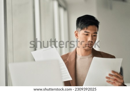 Young busy Asian business man lawyer, tax accountant manager holding paper documents checking bills, doing sales invoice accounting data, reading legal contract or bank statement in office. Royalty-Free Stock Photo #2309392025