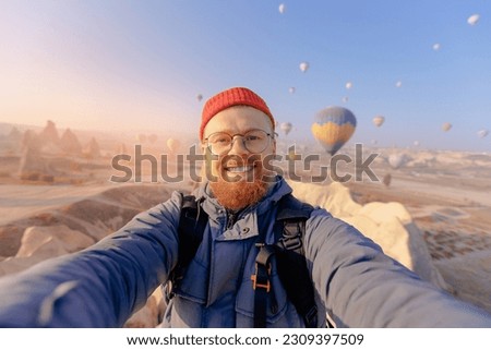 Happy tourist man taking selfie photo in hot air balloon Cappadocia. Concept adventure trip in Turkey.