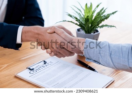 Two business people shake hand after successfully signing contract agreement in corporate office with legal document and pen on the table symbolizes business partnership and cooperation. Entity