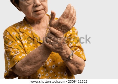 Elderly Asian woman patients suffer from numbing pain in hands from rheumatoid arthritis. Senior woman massage her hand with wrist pain. Concept of joint pain, rheumatoid arthritis, and hand problems.