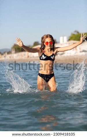 Teenage girl in pink sunglasses having fun on the beach in the sea, playing with waves and splashes. Fun on summer hloiday concept.