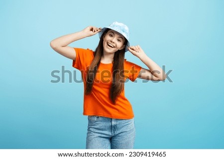 Portrait of cute positive girl in panama hat, wearing orange t shirt, looking at camera isolated on blue background. Summer concept, positive lifestyle