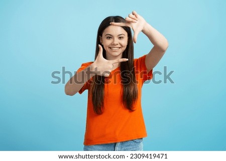 Portrait of attractive teenage girl wearing orange t-shirt showing frame of fingers, gesturing isolated on blue background, copy space