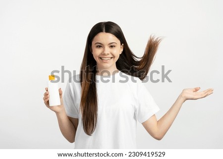 Beautiful smiling teenage girl with long hair holding shampoo isolated on white background. Hair care concept
