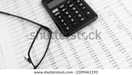 Calculator, keyboard, magnifying glass, eye glasses lying on financial statement. Top view.