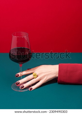 Cropped anonymous person in red clothes with well cared hand and manicured nails holding glass of wine over two color background. Wine shop, wine tasting, bar, wine list concept. Refreshment drink. Royalty-Free Stock Photo #2309490303