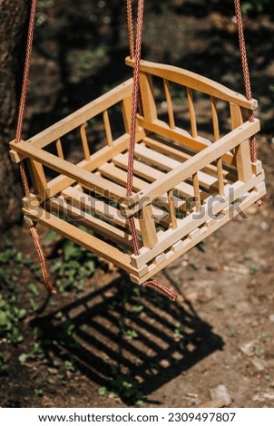 A children's homemade wooden swing made of boards hangs on a rope outdoors in the backyard garden. Close-up photography, childhood.