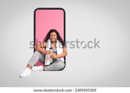 Positive plus size black woman with towel and bottle of water sitting in phone screen isolated on grey studio background, collage, free space. App for training, body care, sports blog