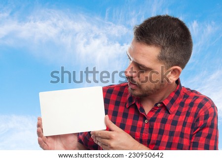 Young man with squares shirt over clouds background. Looking into a white card