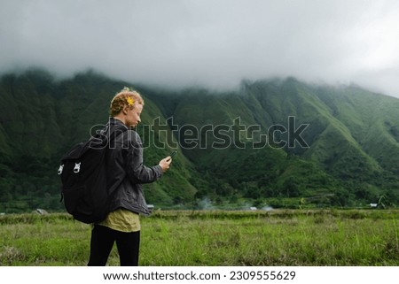 A girl with a backpack travels through the mountains and takes pictures of the surroundings on her mobile phone.