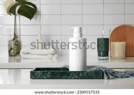 Front view of cosmetic bottle unlabeled placed on marble tray with gray towel, in the background is toiletries, reed diffuser bottle and small potted. Mockup scene for advertising and branding product Royalty-Free Stock Photo #2309557535
