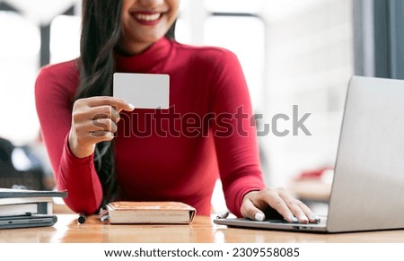 Woman holding blank business card for mock up, using laptop doing online banking.