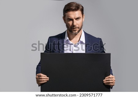 Serious man holds the sign, blank card. Placard ready for your product. Sign to your text. Handsome man showing blank sign board over studio background. Empty blank board. Area advertising.