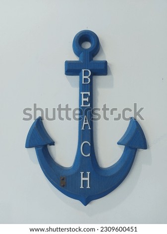a blue anchor with the text 'beach' hangs on a white wall.  isolated background in white