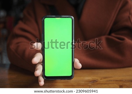 Holding Blank Cell Phone In Hand Showing Green Screen To Camera 