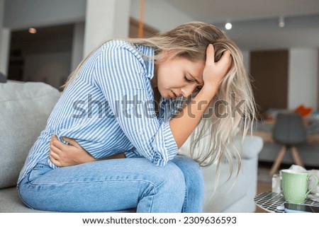 Woman in painful expression holding hands against belly suffering menstrual period pain, lying sad on home bed, having tummy cramp in female health concept Royalty-Free Stock Photo #2309636593