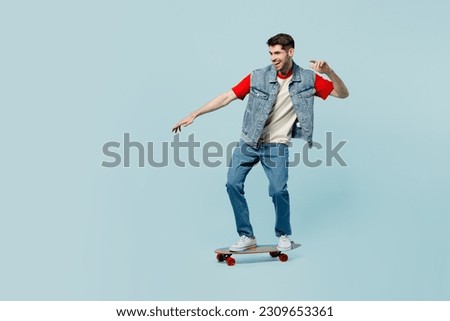 Full body side view active young man he wear denim vest red t-shirt casual clothes riding skateboard pennyboard isolated on plain pastel light blue cyan background studio portrait. Lifestyle concept