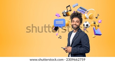 Smiling young African businessman holding smartphone with entertainment icons, video games, streaming music and photos. Concept of online shopping, fun and mobile app. Yellow background, copy space
