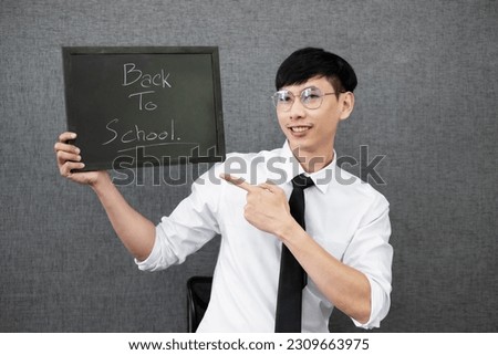 Image of Asian male teacher is holding a blackboard and standing in the classroom on back to school concept.
