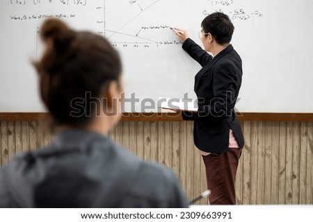 Asian male teacher is standing in front of the classroom and teaching with students listening attentively. School learning and teaching concept.
