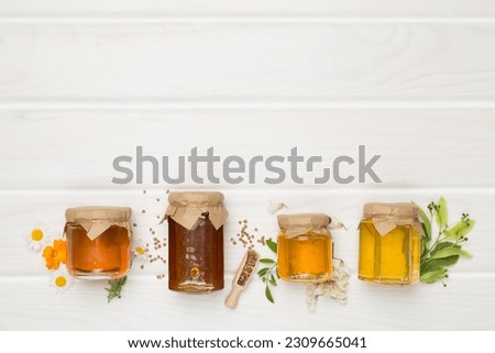 Jars with different types of honey on wooden background, top view