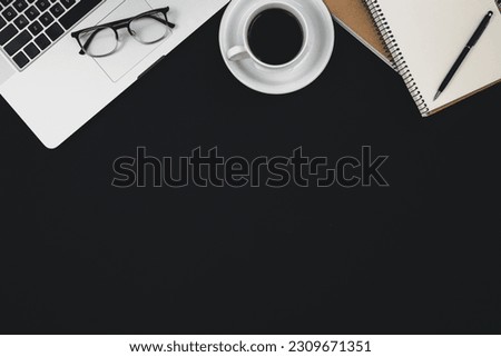 Black background with laptop, notepads, coffee cup and glasses.