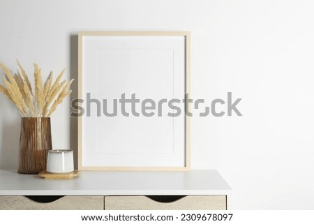 Empty photo frame, cup and vase with dry decorative spikes on white table. Mockup for design