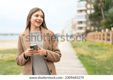 Young pretty blonde woman using mobile phone and looking up