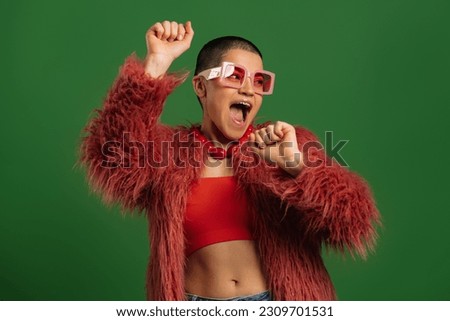 Joyful young short hair woman in trendy clothes dancing against green background