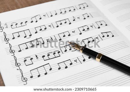Sheet with musical notes and fountain pen on table, closeup