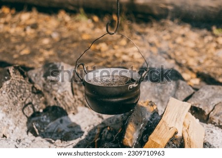 Hiking pot, Bowler in the bonfire. soup boils in cauldron at the stake. Traveling, tourism, picnic cooking, cooking at the stake in a cauldron, fire and smoke.