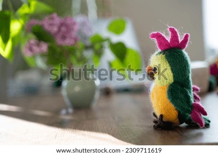 knitted toy parrot on the table with lilac flowers