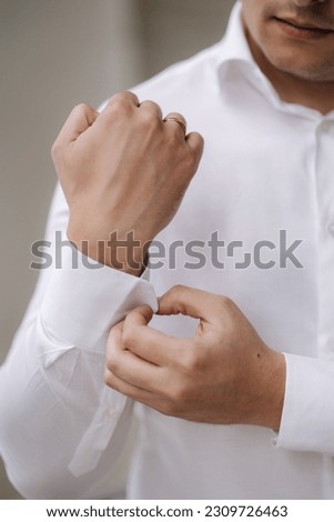 Photo of man fastens the cufflink on the shirt sleeve. Grooms morning on wedding. Close-up