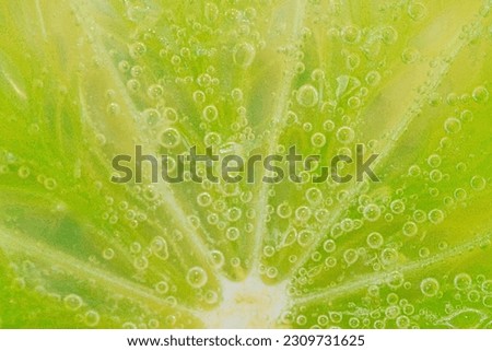 Slice of ripe lime in water. Close-up of lime in liquid with bubbles. Slice of ripe lime in sparkling water. Macro horizontal image of fruit in carbonated water. Detail of lime slice with bubbles. Royalty-Free Stock Photo #2309731625