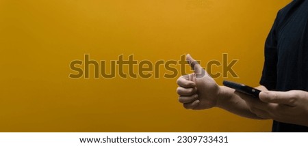 Man holding smartphone and showing thumb up isolated on yellow background with copy space for text