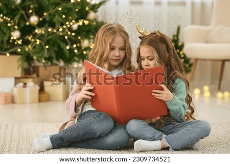 Cute little girls reading book at home. Christmas atmosphere