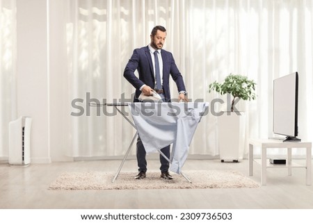 Businessman ironing a shirt at home in front of tv in a living room