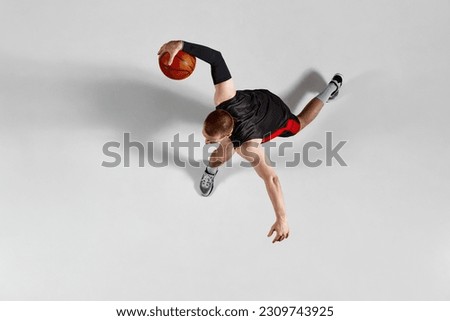 Dynamic image of professional sportsman, basketball player in motion with ball during game against grey studio background. Top view. Concept of professional sport, hobby, healthy lifestyle, action