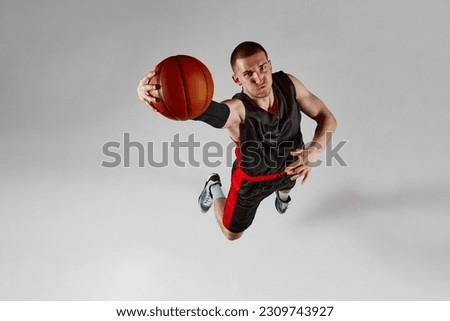 Concentrated sportsman, male basketball player in motion, jumping with ball against grey studio background. Top view. Slam dunk. Concept of professional sport, healthy lifestyle, action and motion