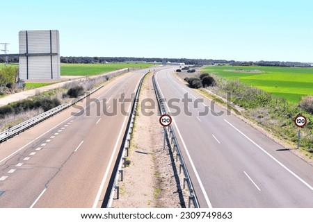 Photograph of a highway with almost no traffic, with a curve in the distance, sunny day, blue sky and no clouds. Speed limit signs. Photograph with a high angle of view. Selective focus. Copy space