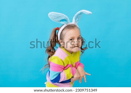 portrait of a little girl with rabbit ears in a striped jacket. The concept of the Easter holiday. Blue background, photo studio, place for text