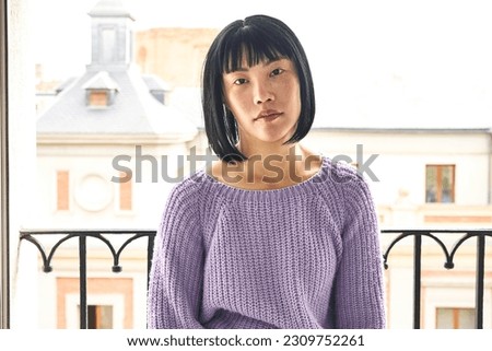 Subtly posing, a young Asian woman enhances her inherent beauty on the balcony.