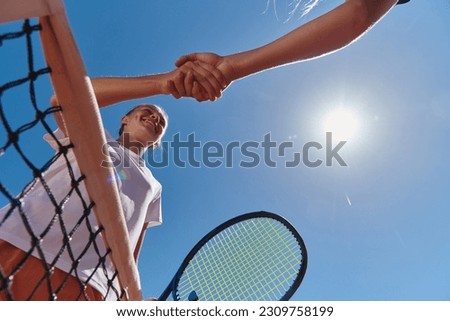Two female tennis players shaking hands with smiles on a sunny day, exuding sportsmanship and friendship after a competitive match. Royalty-Free Stock Photo #2309758199