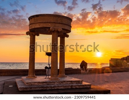 beautiful stone monument with three columns in ancient history greek style with see embarkment and amazing cloudy sunset on background of landscape with seashore and water