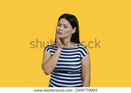Young asian woman is touching her cheek suffering from toothache. Isolated on yellow.