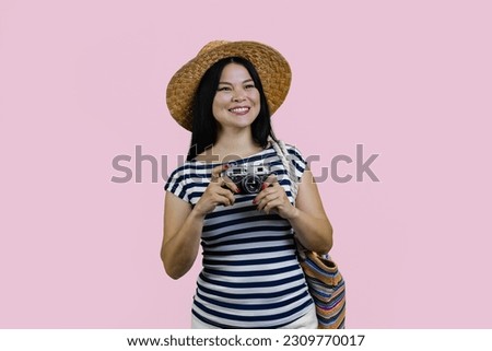 Portrait of a happy young brunette asian female tourist with retro vintage photo camera. Isolated on pink background.