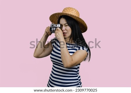 Young brunette asian female tourist taking a photo on retro photo camera. Isolated on pink background.