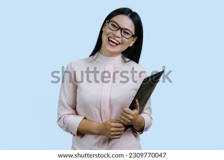 Young asian laughing woman in glasses with clipboard. Isolated on pale blue.